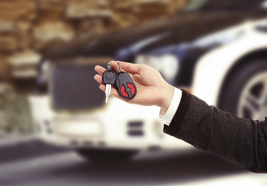 Male hand holding car keys on car background